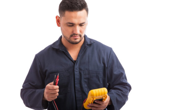 Young male electrician checking voltage using a multimeter on a white background